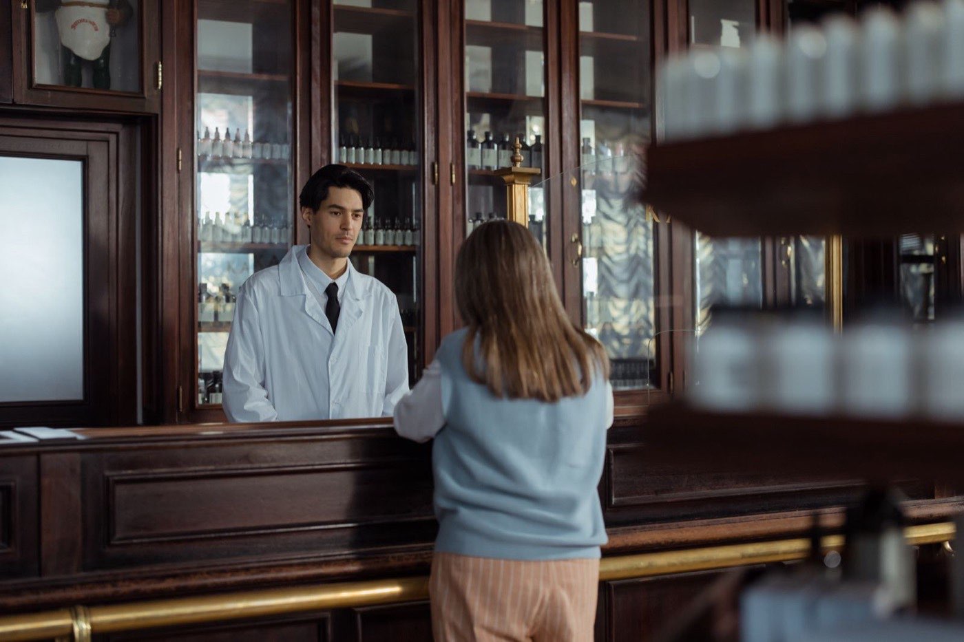 Een apotheker in witte jas helpt een klant aan de houten balie van een klassieke apotheek