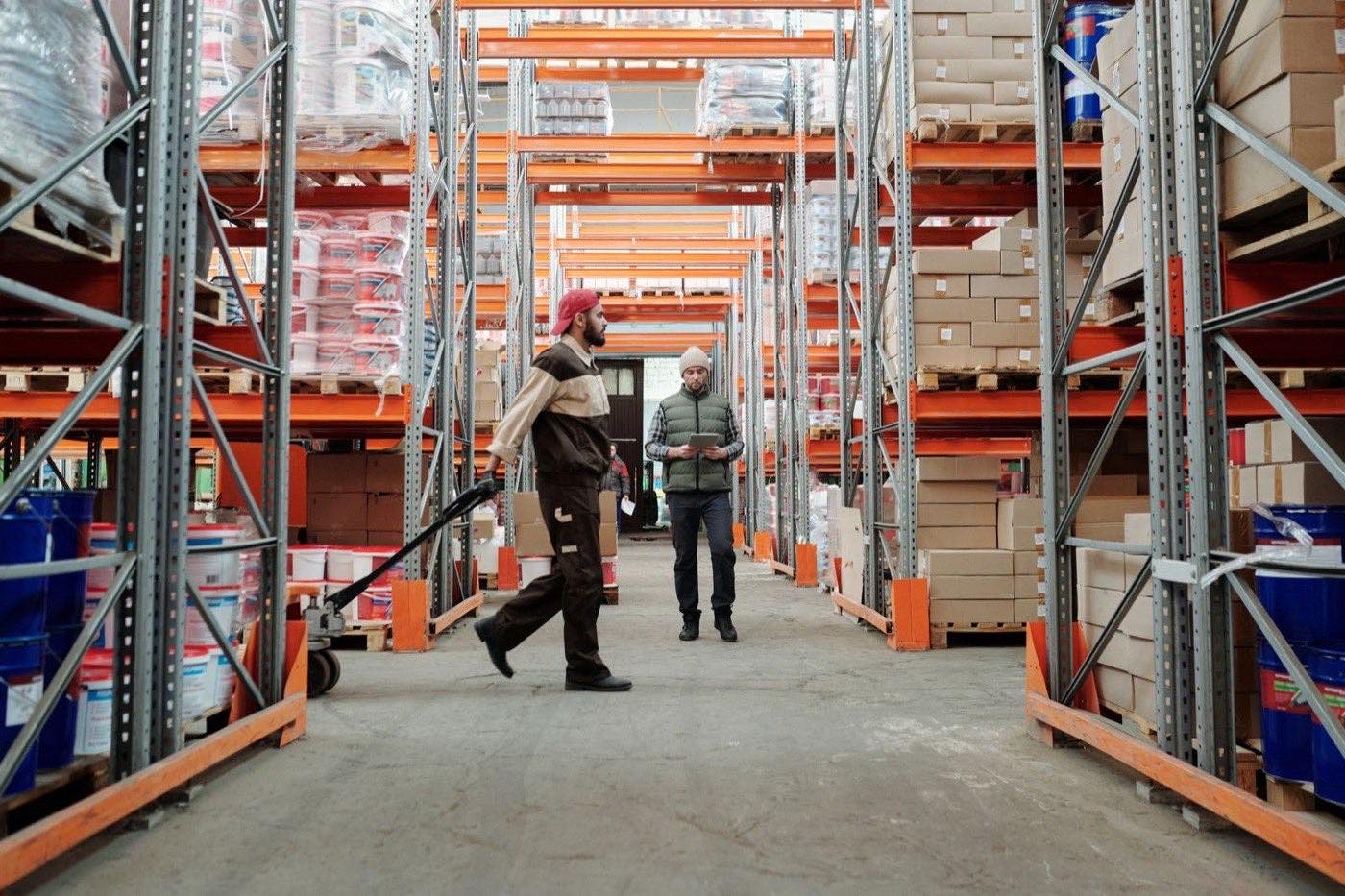 Twee magazijnmedewerkers tussen hoge stellingen met palletrekken